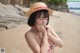 A woman in a straw hat sitting on a beach.