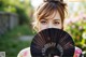 A woman holding a black fan in front of her face.