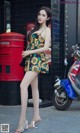 A woman standing next to a red post box on a city street.