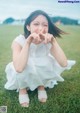 A woman in a white dress sitting on the grass making a peace sign.